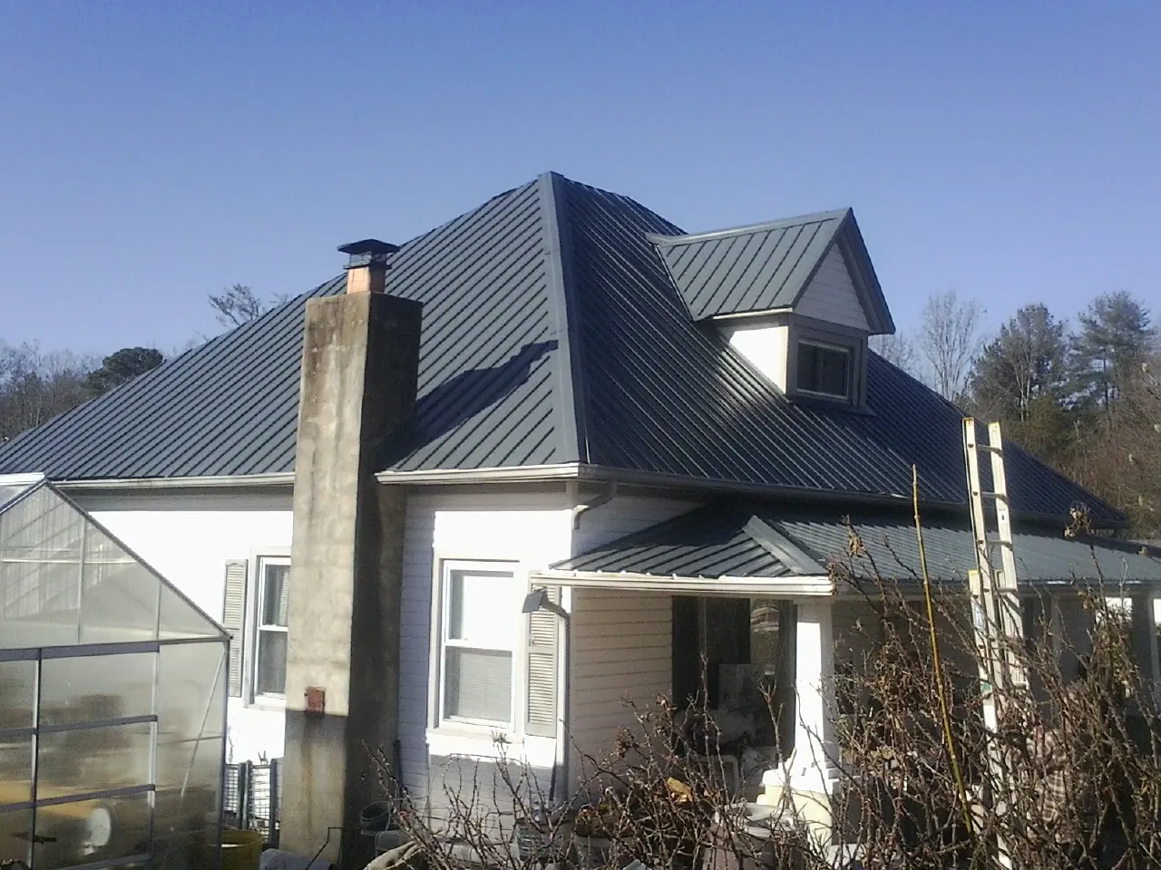 Dark blue standing seam metal roof on a white farmhouse with dormer — Slate & Tile Roof Repair by Roofing Brothers in New Deal