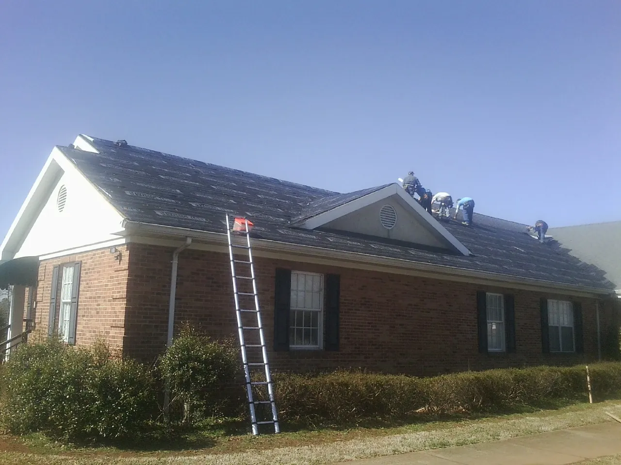 Crew tearing shingles off a brick ranch roof with a ladder set — Emergency Roof Repair work by our crew in New Deal