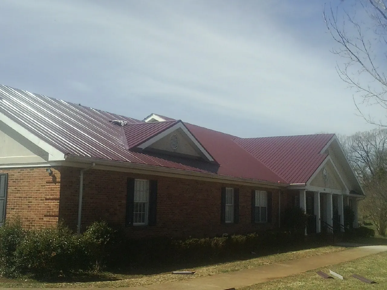 Red metal roof with gabled entries on a long brick building, from a Hail Damage Roof Repair job in New Deal