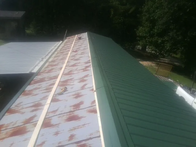 Old rusted panels beside newly installed green metal roofing — Wind Damage Roof Repair by Roofing Brothers in New Deal