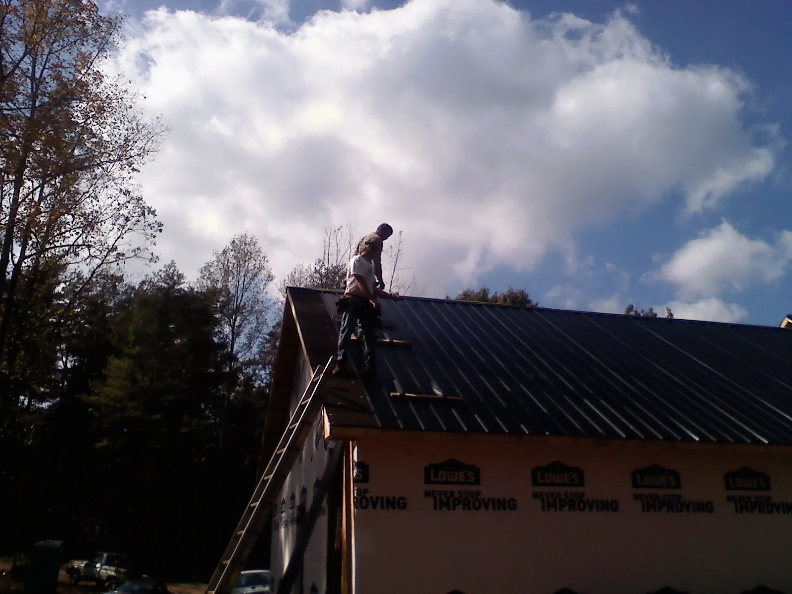 Roofer fastening dark metal panels high against a cloudy sky, from a Roof Inspection job in New Deal
