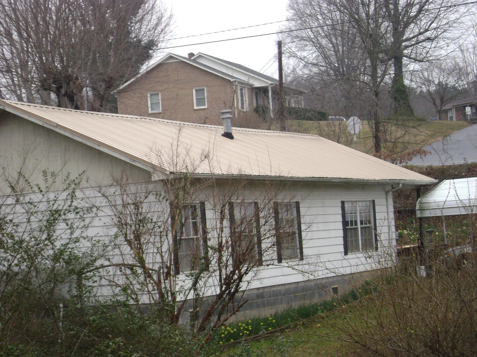 Tan metal roof on a white sided house set into a hillside — Commercial Roofing by Roofing Brothers in New Deal